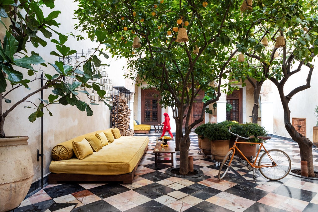 Elegant Moroccan hotel courtyard with emerald pool, pink walls, ornate archways, and traditional lanterns casting warm evening light