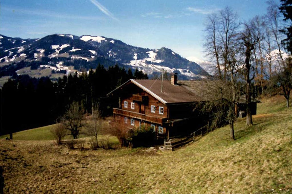 Traditional Alpine hotel with wooden balconies and white exterior, nestled against snow-capped mountains and pine forests at sunset