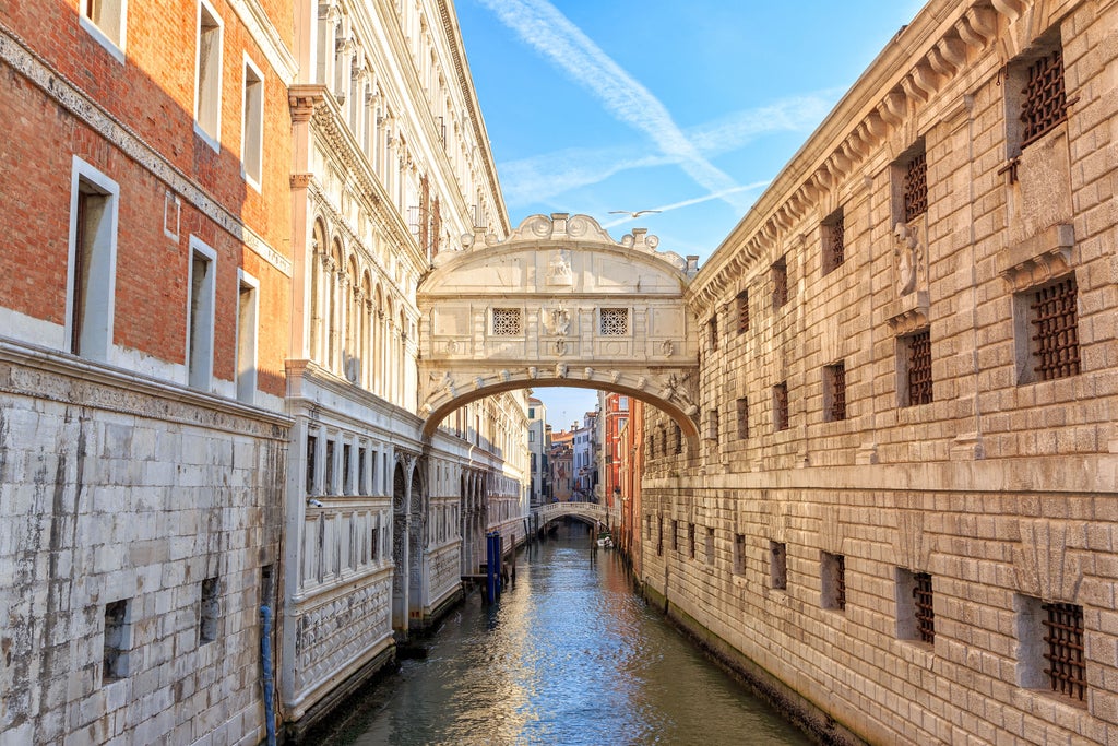 Ornate Venetian palace facade with Gothic windows and marble columns reflects in calm canal waters at golden hour sunset