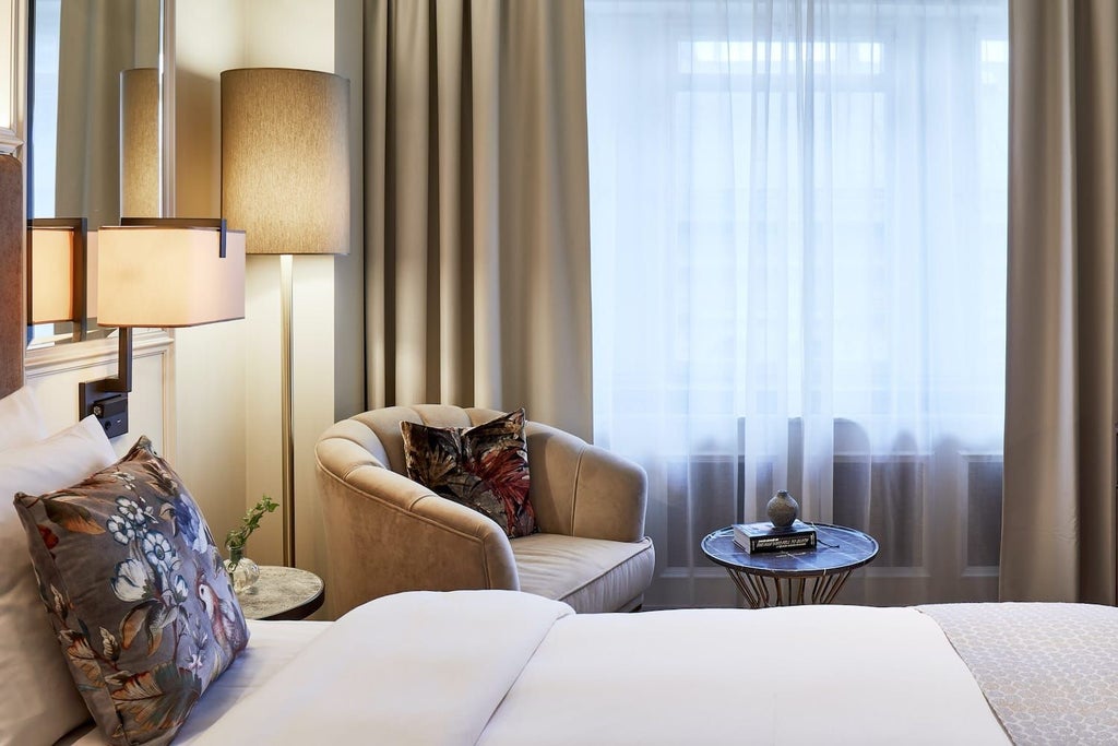 Luxurious classic hotel room in neutral tones with plush cream armchair, ornate wooden furnishings, and elegant chandelier against refined Swedish design aesthetic