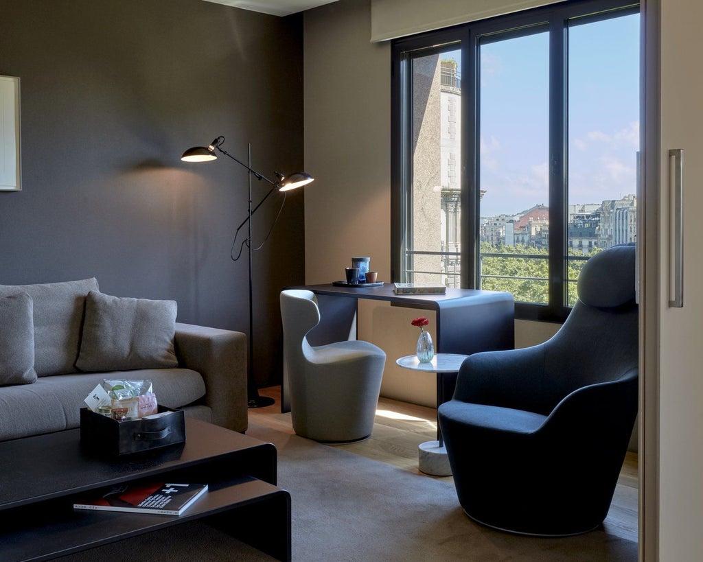 Elegant modern hotel suite with minimalist design, panoramic urban view, sleek neutral tones, and floor-to-ceiling windows overlooking a Spanish cityscape