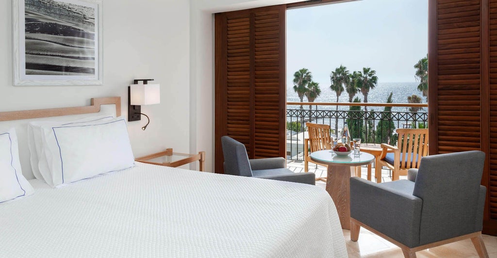 Spacious two-bedroom suite with elegant modern decor, plush white beds, marble bathroom, and panoramic windows overlooking Mediterranean coastal scenery.