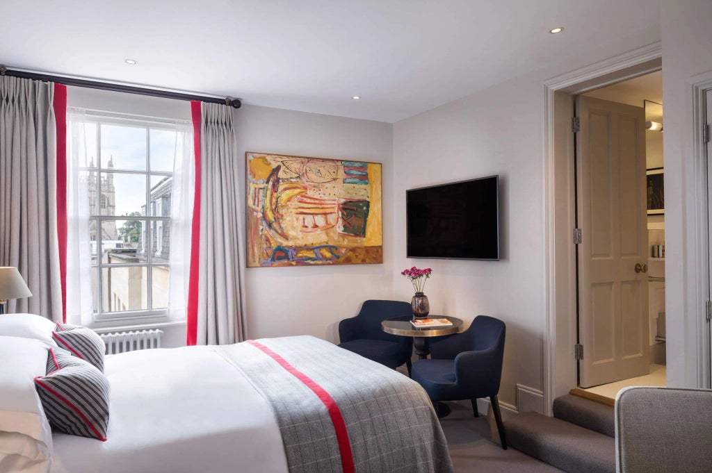 Elegant classic hotel room with mahogany furnishings, crisp white linens, and large windows overlooking historic UK architecture in warm afternoon light