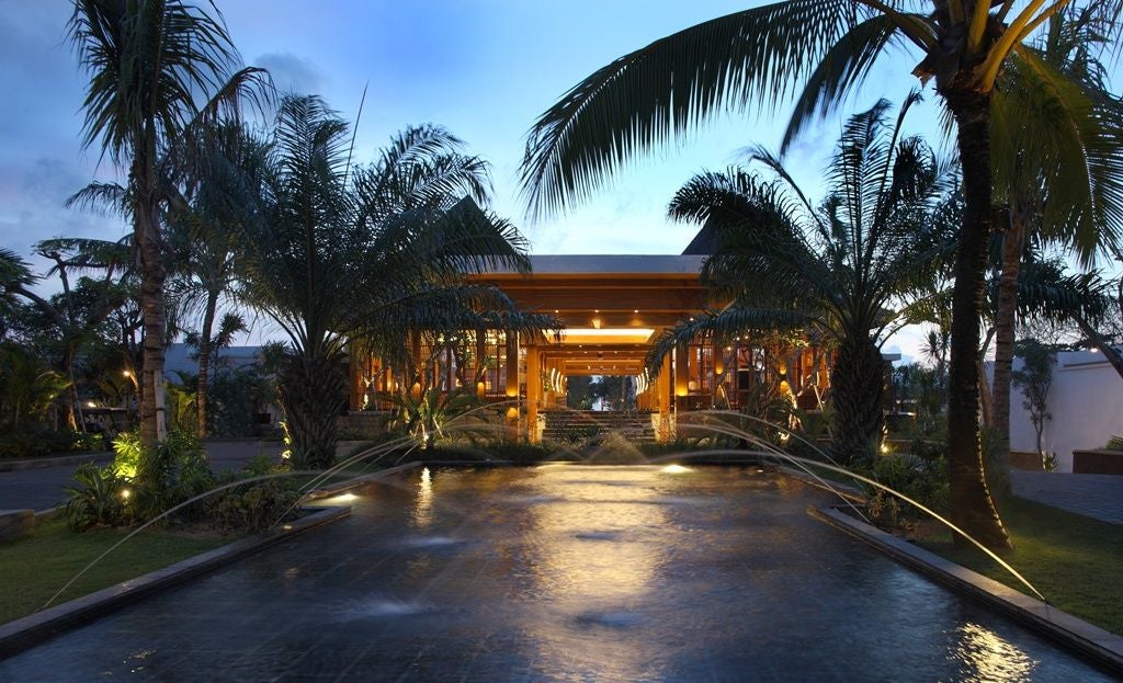 Luxurious infinity pool overlooking lush Balinese jungle, with contemporary white loungers and traditional thatched-roof pavilions