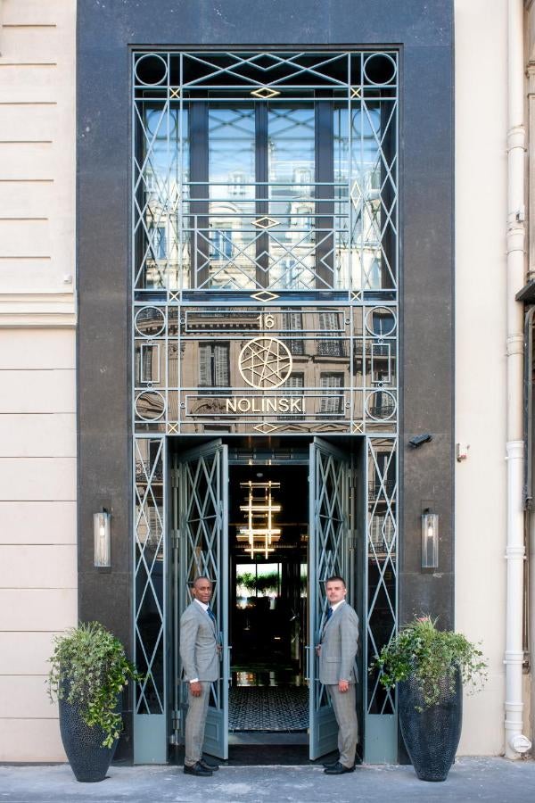 Elegant Parisian hotel facade with ornate stone carvings, wrought-iron balconies, and classic windows illuminated at dusk in soft golden light