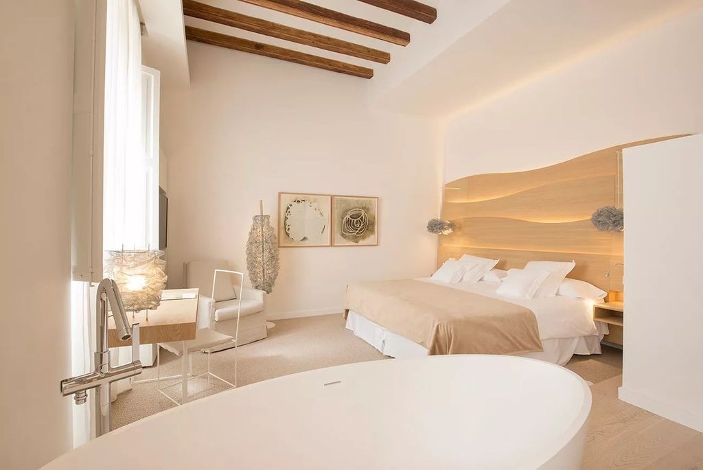 Elegant junior suite with minimalist design, white marble floors, king-size bed, modern artwork, and soft natural light in historic Spanish hotel conversion