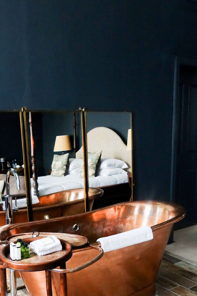 Elegant four-poster bed with rich burgundy linens, ornate wooden furnishings, and soft mood lighting in luxurious Kings Head Hotel room in United Kingdom