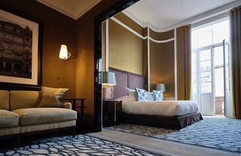 Elegant suite with plush cream-colored furnishings, ornate gold-framed artwork, and classic Portuguese architectural details in luxurious hotel room