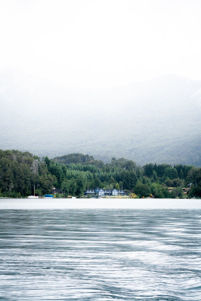 Luxurious lakeside resort with wooden pier stretching into calm waters, flanked by snow-capped Patagonian mountains at sunset