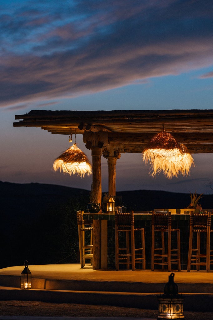 Desert glamping suite at Caravan Agafay with white canvas tent, outdoor terrace, modern furniture against rugged Atlas Mountains backdrop