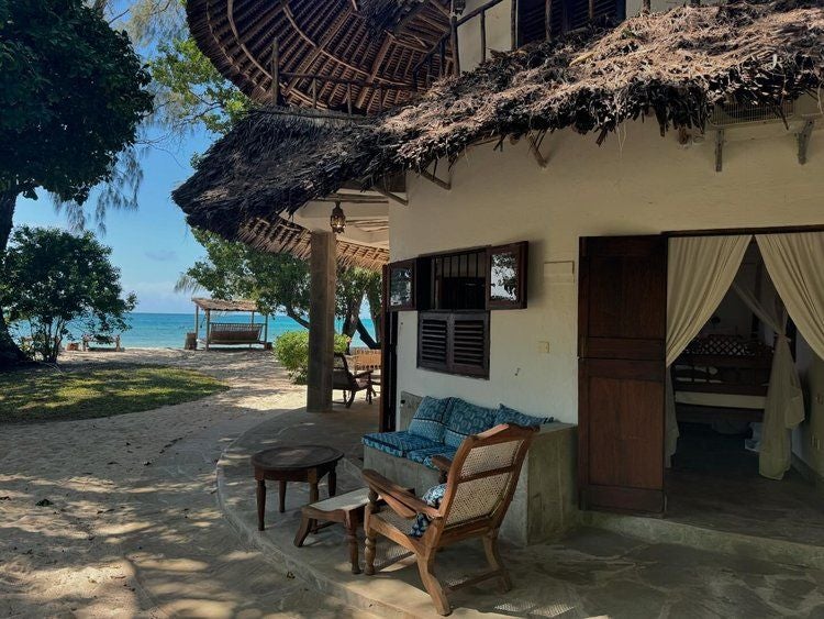 Luxurious beachfront resort with white sandy beach, tropical palm trees, and elegant Swahili-style architecture overlooking the turquoise Indian Ocean in coastal Kenya