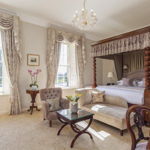 Elegant grand suite at luxury countryside hotel, featuring opulent four-poster bed, rich cream and gold color palette, and classic period furnishings