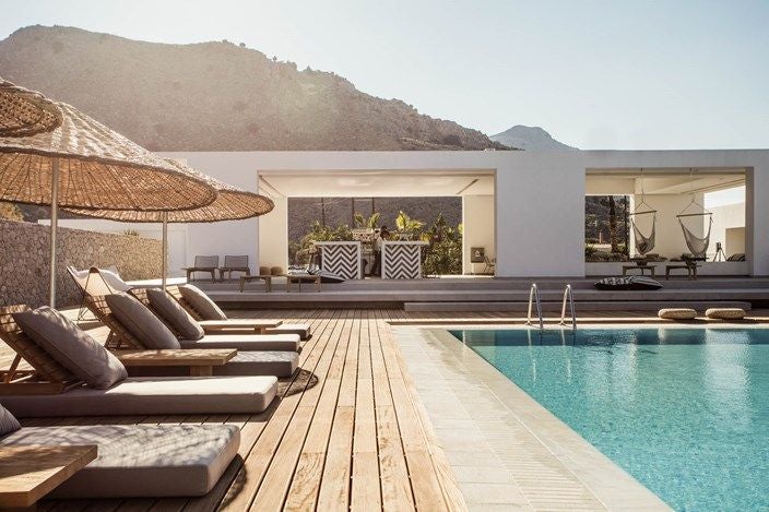 Private white-washed villa with turquoise infinity pool overlooking Mediterranean landscape, modern lounge chairs and tropical plants at dusk