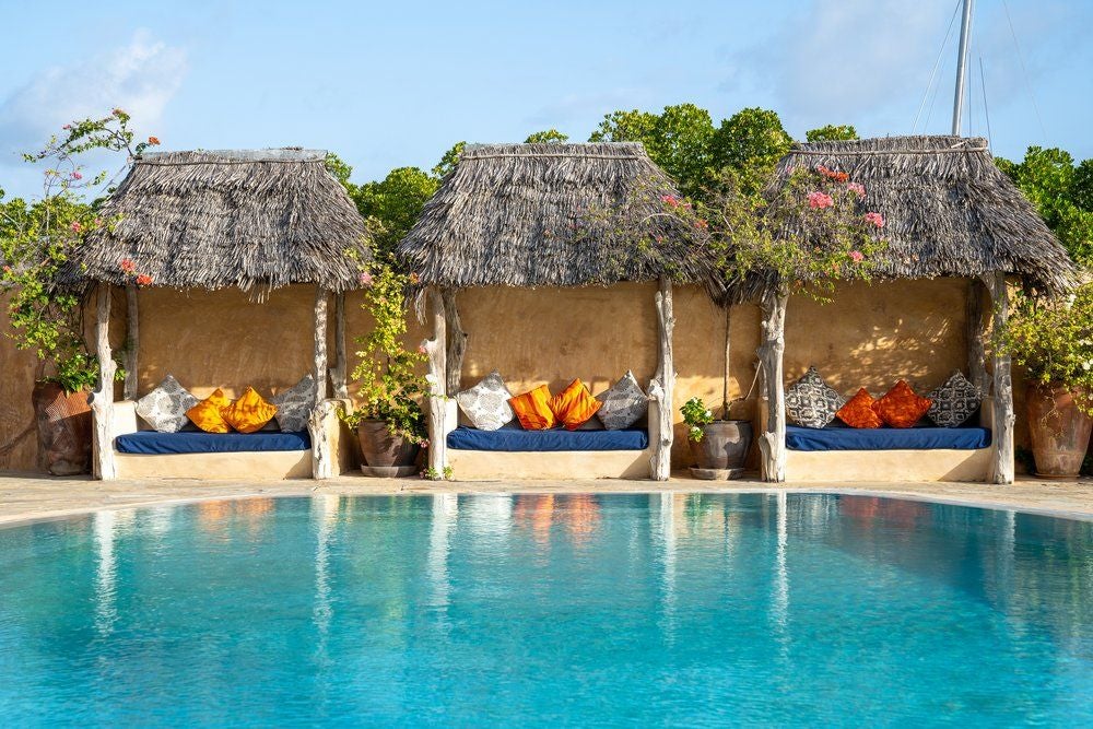 Beachfront luxury thatched-roof cottage at Manda Bay resort, nestled among palm trees with private veranda overlooking turquoise Kenyan waters