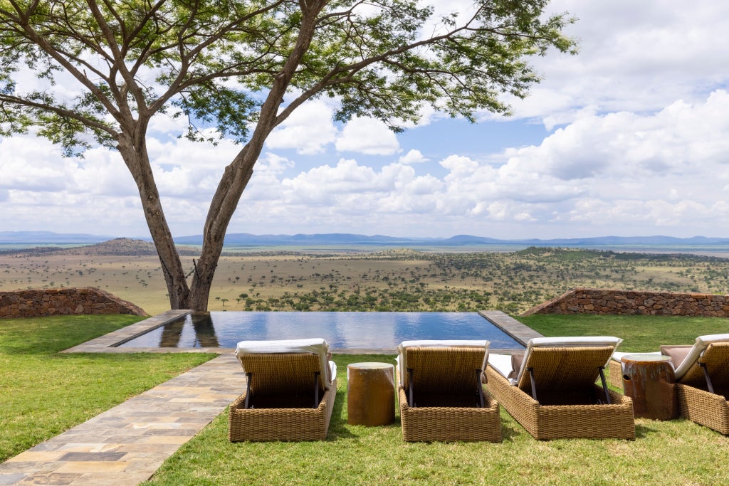 Elegant stone lodge with infinity pool overlooking vast African savanna, featuring colonial-style architecture and manicured gardens