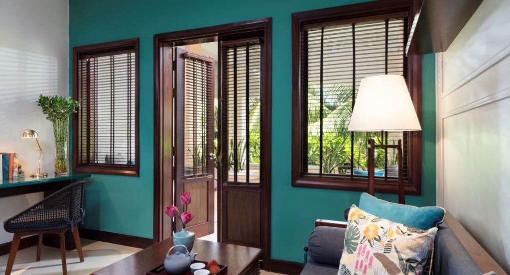 Elegant hotel room with river-view balcony featuring king bed, teak furnishings, marble bathroom and traditional Vietnamese decor