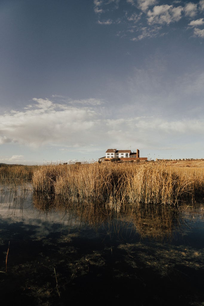 Modern luxury lodge built on stilts over Lake Titicaca with stone-clad walls, panoramic windows, and dramatic mountain backdrop at sunset