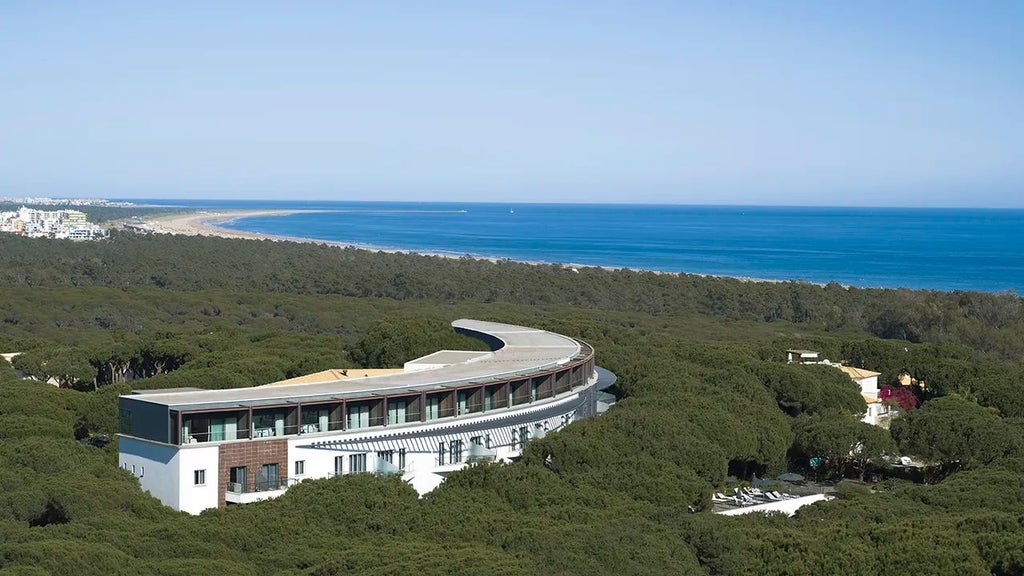 Luxurious Portuguese coastal resort with white minimalist architecture, blue pool, and lush greenery overlooking a pristine sandy beach at Scenset Verde