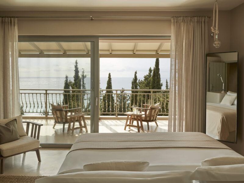 Minimalist white bedroom with wooden accents, King sized bed, sea-view window, soft neutral tones, modern Greek island luxury retreat design in F Zeen Kefalonia