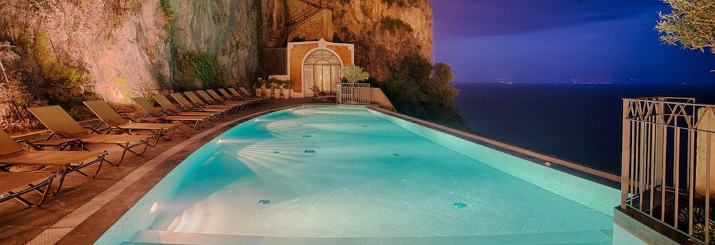 Historic luxury hotel carved into Amalfi Coast cliffs with infinity pool overlooking Mediterranean Sea and traditional Italian architecture