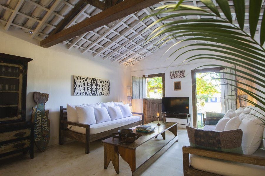 Rustic wooden-beamed luxury suite at UXUA Casa Hotel and Spa, featuring traditional Brazilian design with minimalist white linens and warm tropical ambiance