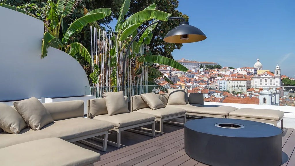 Elegant boutique hotel terrace overlooking Lisbon's historic Alfama district, with traditional red-tiled roofs and warm sunset hues in the background