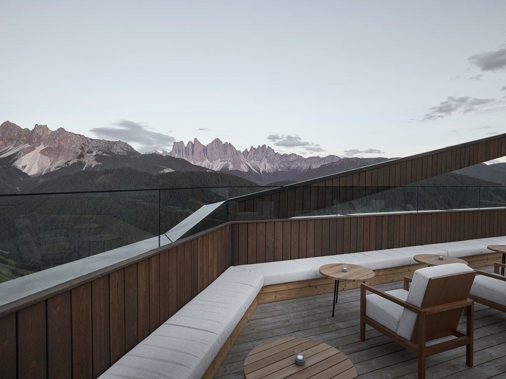 Modern mountain resort with floor-to-ceiling windows reflecting snow-capped Dolomites, featuring minimalist wood and stone architecture