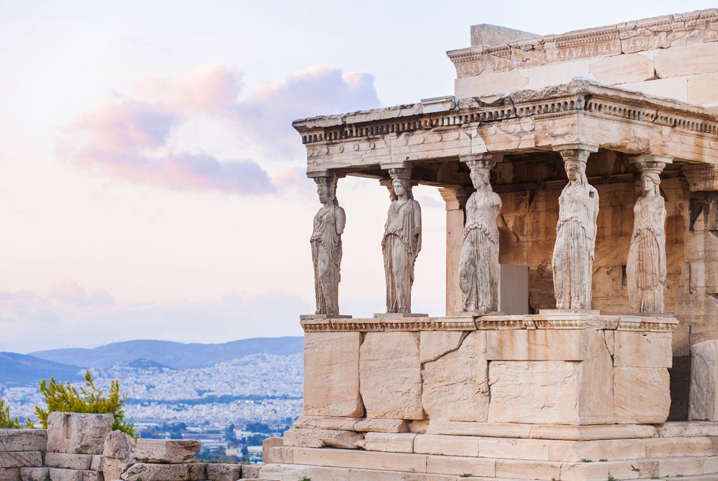 Ancient Acropolis and Parthenon temple perched on hilltop at sunset, overlooking modern Athens cityscape with luxury hotels below