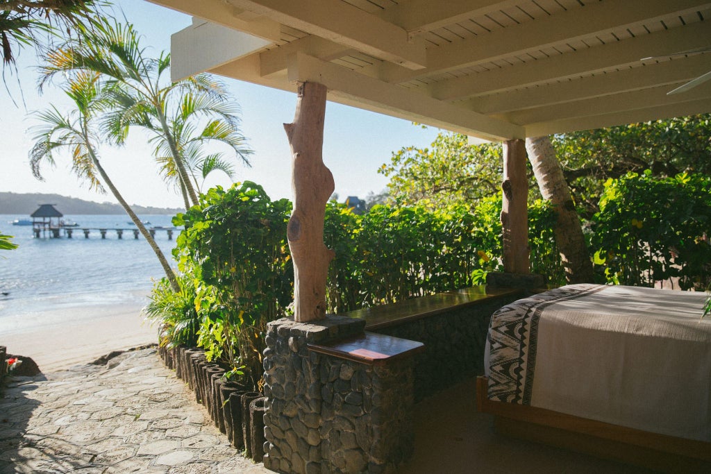 Luxurious Fijian water's edge villa with panoramic ocean view, private deck, traditional thatched roof, and lush tropical surroundings at sunset