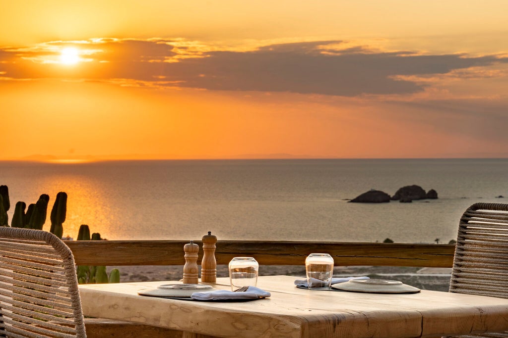 Whitewashed luxury hotel with infinity pool overlooking Santorini's caldera, blue-domed churches and Aegean Sea at sunset