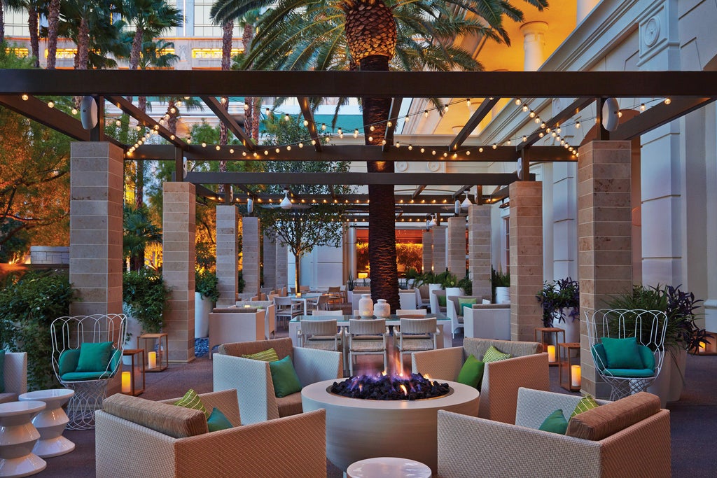 Elegant curved glass tower of Four Seasons Las Vegas set against clear blue sky, with palm trees and pristine landscaping in foreground