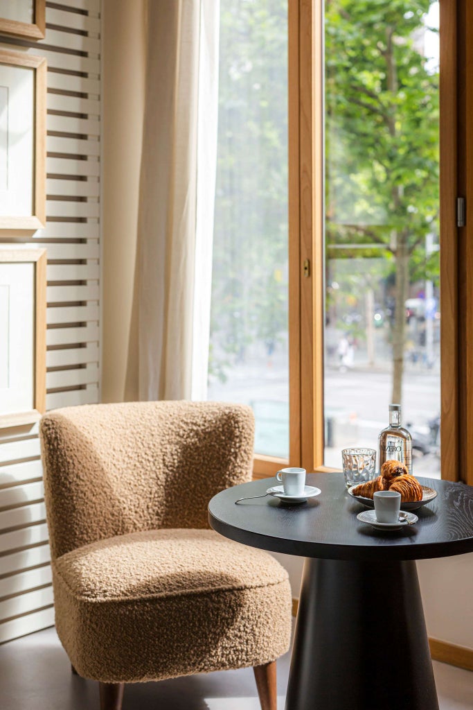 Elegant Barcelona hotel room with plush white bedding, minimalist decor, large windows, and warm wooden accents in a sophisticated deluxe suite