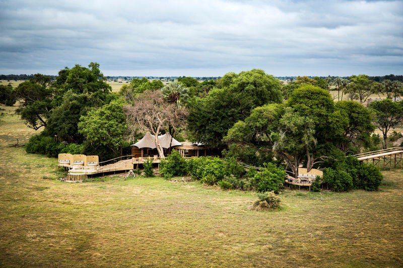 Elevated luxury safari lodge with tented suite and wooden deck overlooking vast grassland plains of the Okavango Delta at sunset