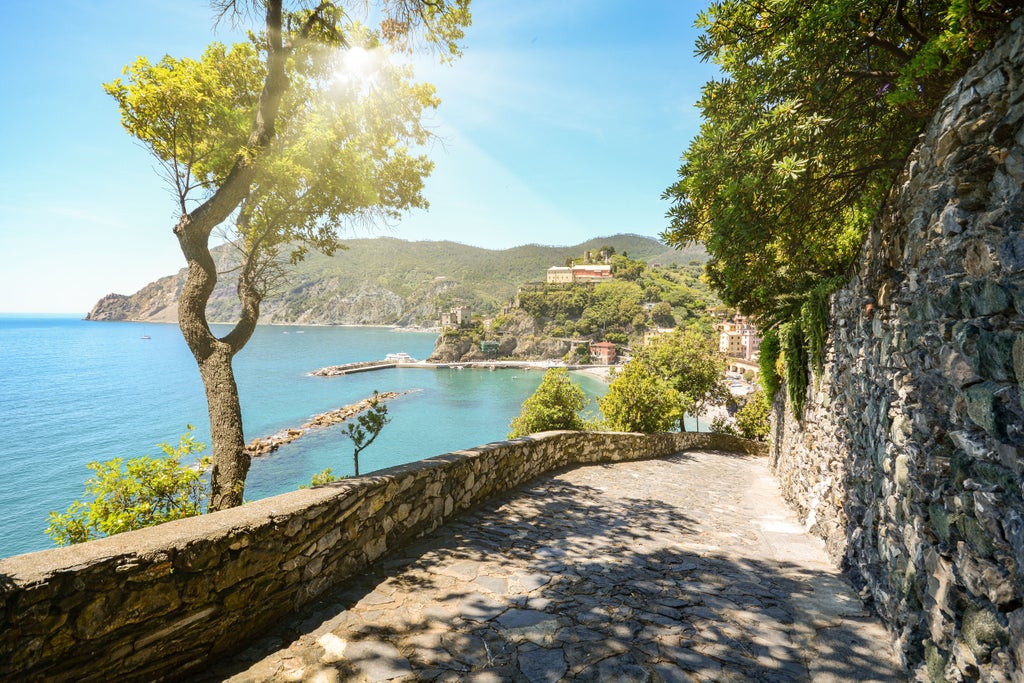 Hikers traverse a scenic coastal trail with stone steps overlooking the turquoise Mediterranean Sea leading to San Fruttuoso Abbey