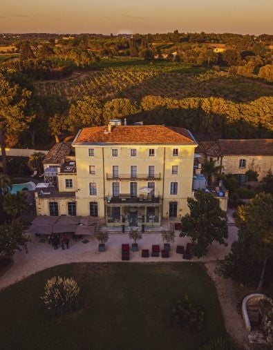 Elegant stone chateau hotel with ivy-covered walls, ornate French windows, and manicured gardens set against a sunset sky in Montpellier