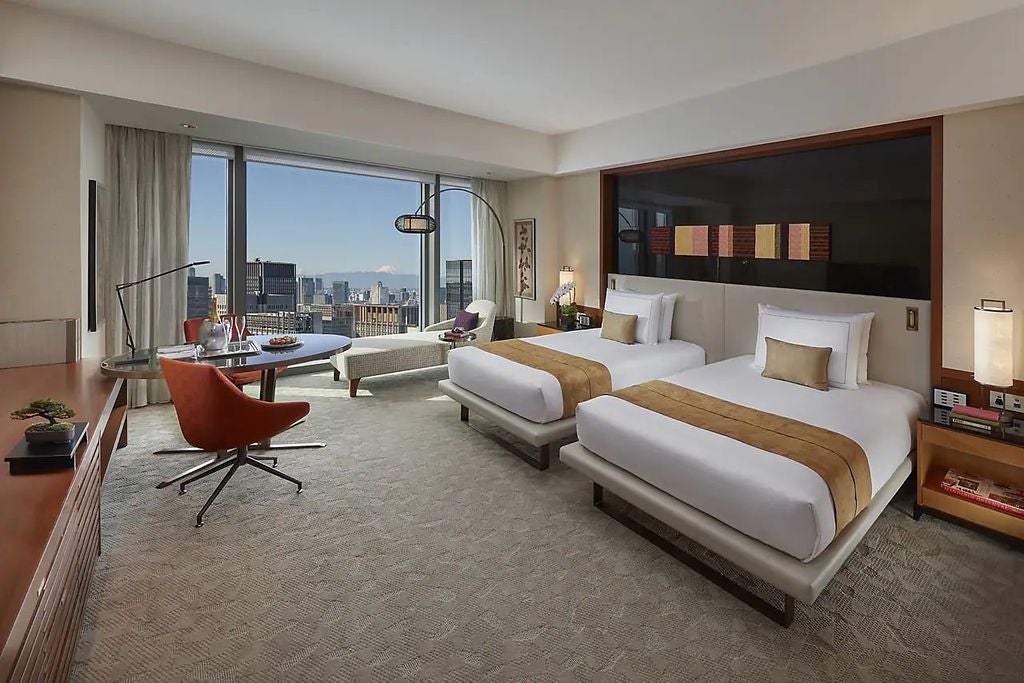 Modern corner suite with panoramic city views, plush king bed, elegant furnishings, floor-to-ceiling windows and warm ambient lighting