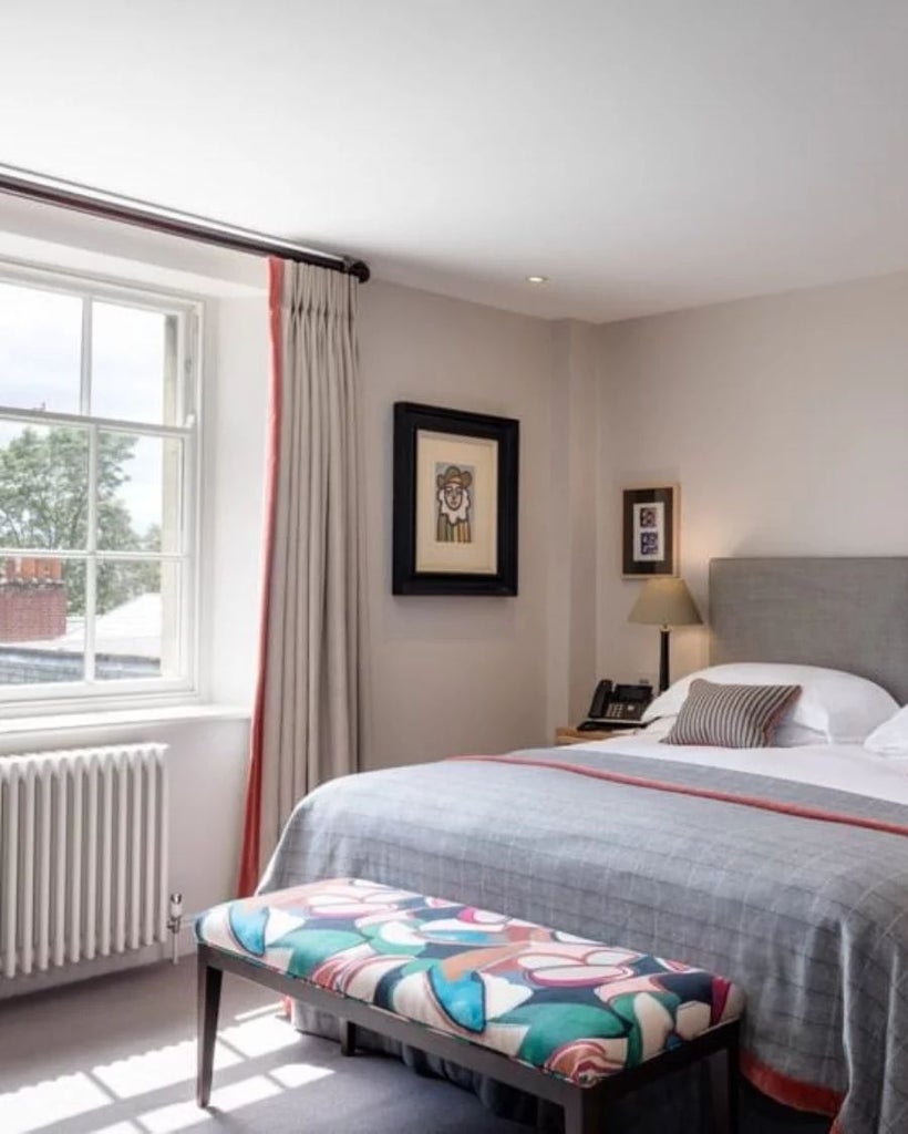 Elegant deluxe hotel room with plush white bedding, soft neutral tones, classic wooden furnishings, and sophisticated artistic decor at Old Parsonage Hotel in UK