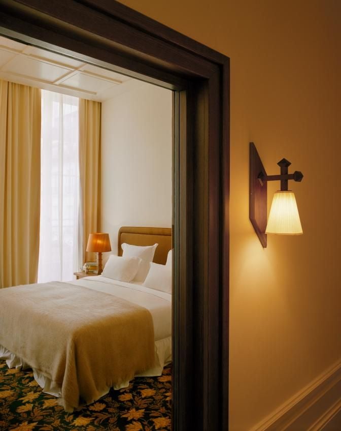 Elegant junior suite at Château Voltaire with plush cream-colored armchair, ornate mirror, soft neutral tones, and delicate French provincial styling