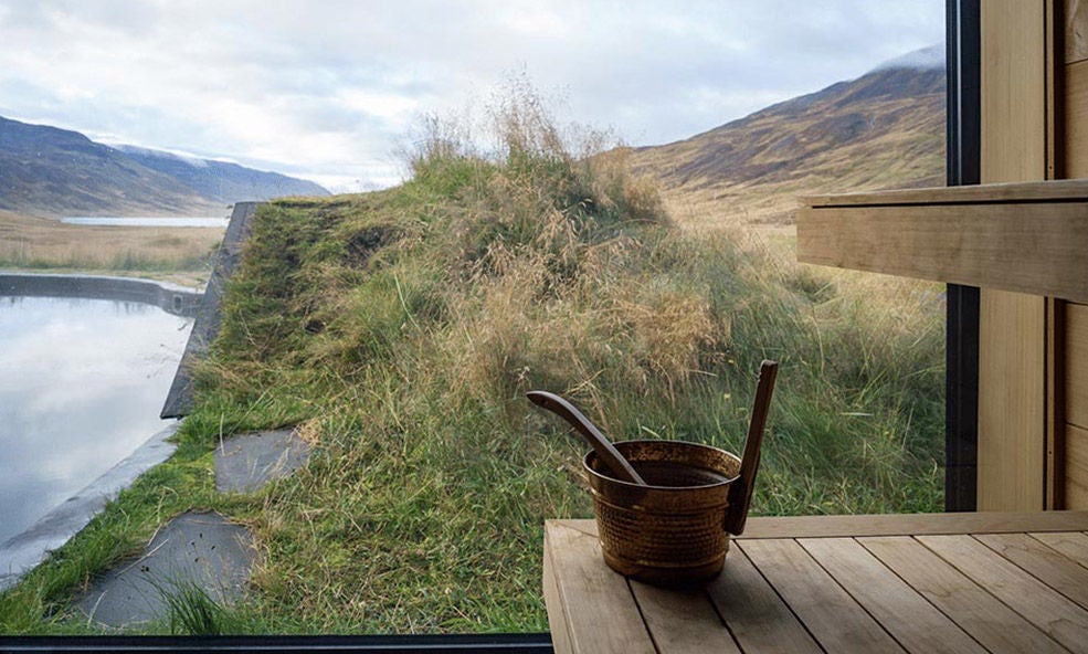 Luxurious black timber lodge Deplar Farm nestled in snowy Icelandic valley, illuminated windows glowing against mountain backdrop