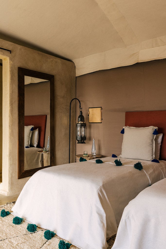 Desert luxury tent with billowing white fabric, stone path leading to raised deck overlooking Moroccan mountains at dusk