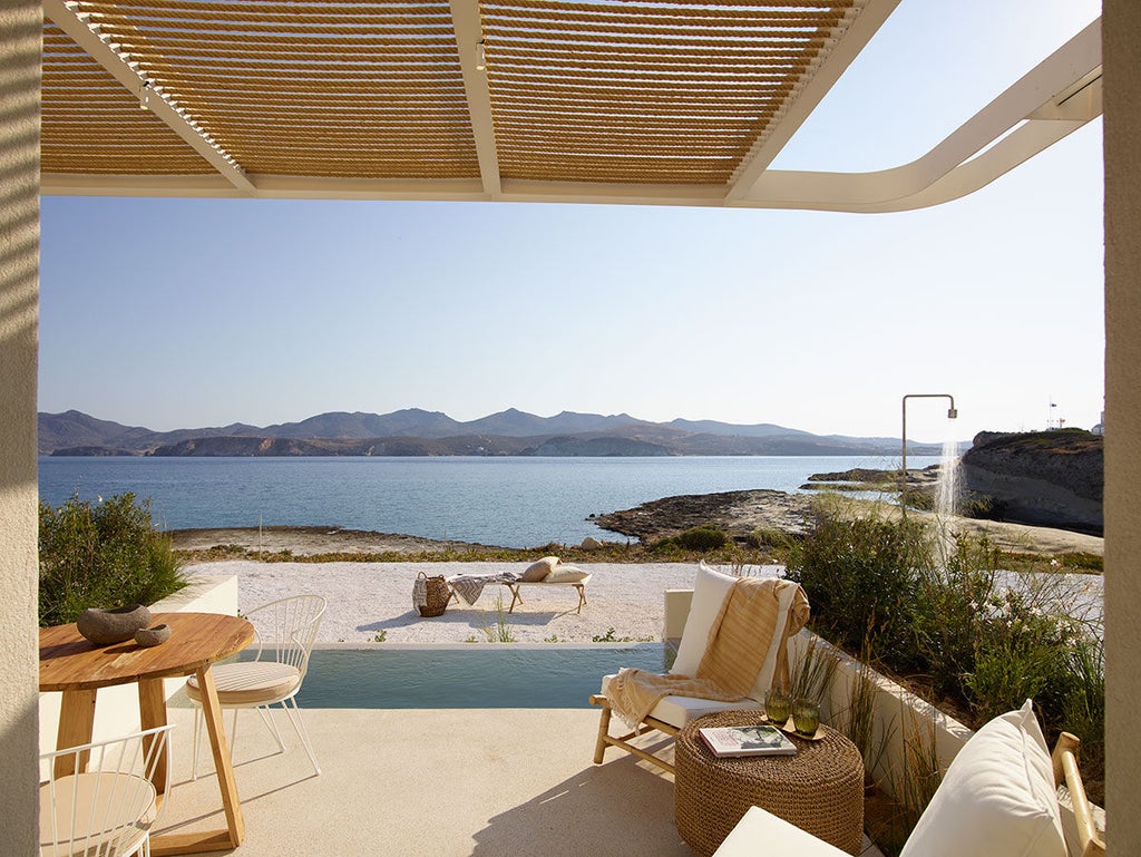 A luxurious white cave suite with private infinity pool overlooking Santorini's caldera, illuminated by warm sunset light