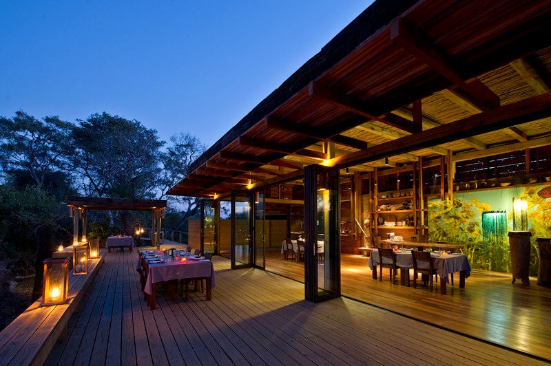 Contemporary safari lodge with raised wooden deck overlooking vast savanna grasslands, featuring luxury tents and private plunge pool