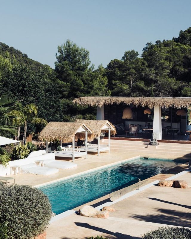 Minimalist white boutique hotel with clean lines, tropical palm trees, and infinity pool overlooking scenic Ibiza landscape at golden hour