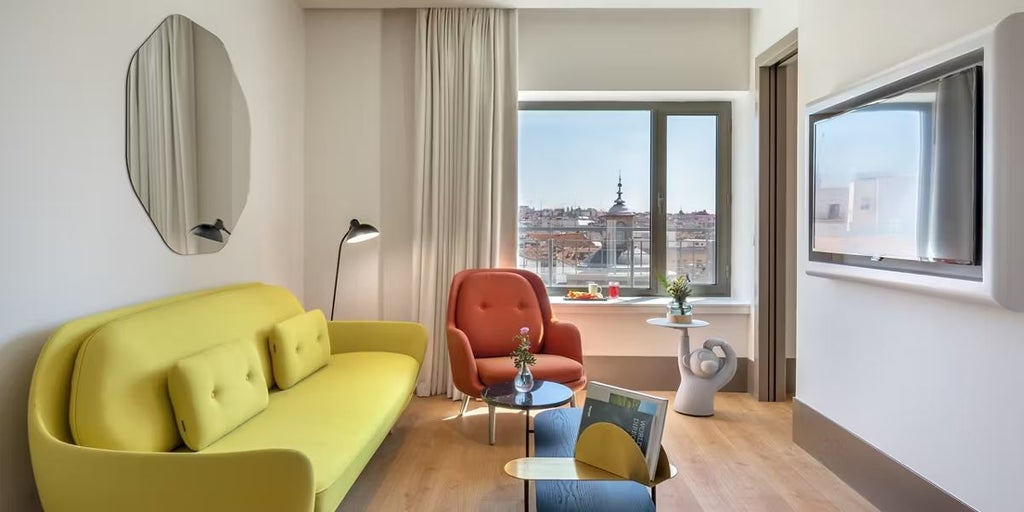 Luxurious princess suite at Barceló Torre de Madrid, featuring elegant cream decor, plush king bed, modern chandelier, and expansive city view windows