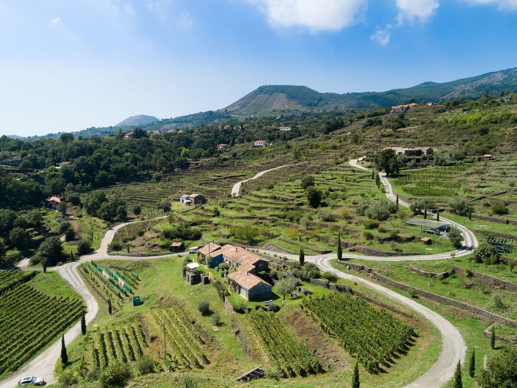 Elegant boutique hotel nestled on Mount Etna's slopes, featuring rustic stone walls, lush gardens and panoramic Sicilian vineyard views