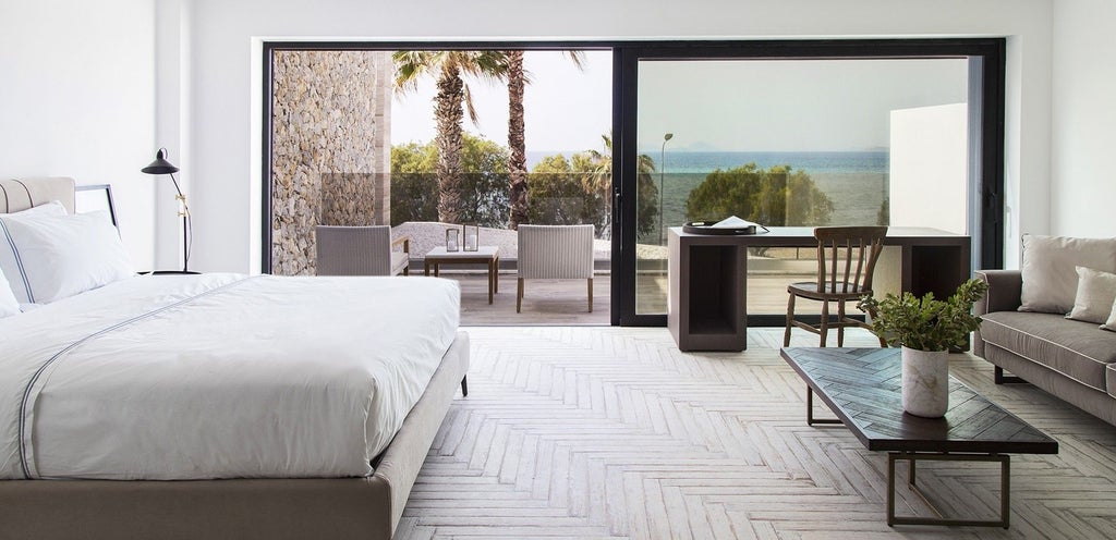 Luxurious minimalist suite with expansive sea view, white modern furnishings, floor-to-ceiling windows, and elegant coastal design at scenic Greek hotel