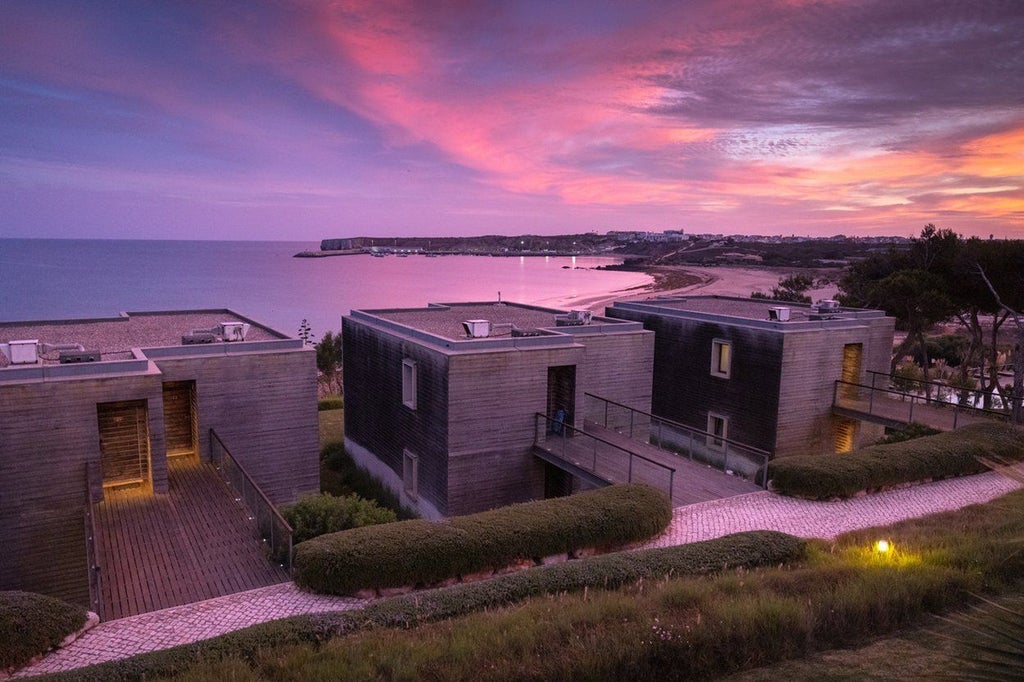 Luxurious coastal resort nestled in Sagres, Portugal, with white-washed buildings, swimming pools, and stunning Atlantic Ocean views at sunset