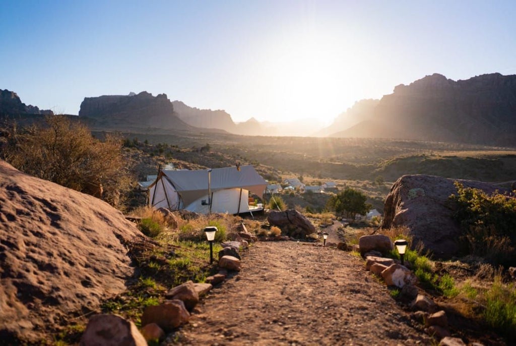 Luxurious safari-style tent nestled against dramatic red rock cliffs of Zion National Park, with warm golden sunset lighting the canvas and landscape