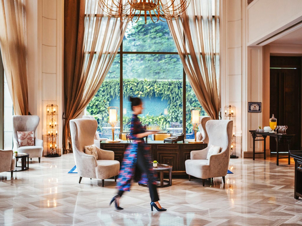 Elegant colonial-style luxury hotel in Saigon featuring white facade, ornate balconies, and tropical landscaping against blue sky