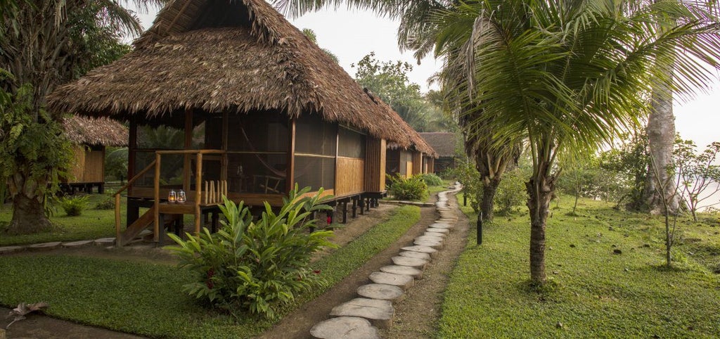 Luxurious treehouse-style cabana with thatched roof and wooden walkways suspended in lush Peruvian rainforest canopy at sunset